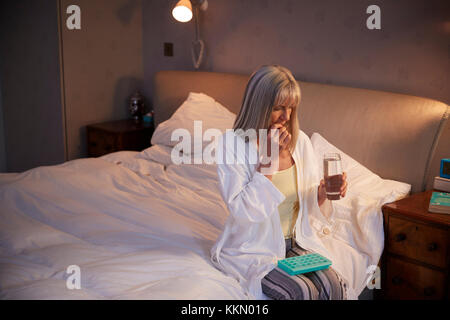 Senior donna seduta sul letto di casa la somministrazione dei farmaci Foto Stock