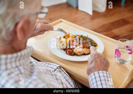 Sulla spalla vista di senior uomo mangiare a cena a casa Foto Stock