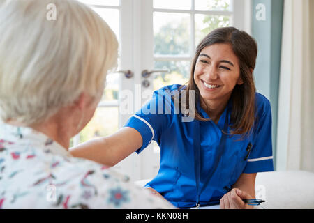 Care giovani infermiere su home visita confortante donna senior Foto Stock