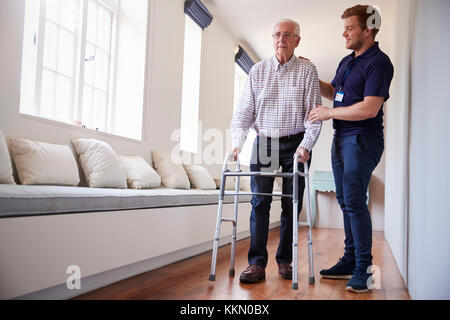 Senior uomo utilizzando un telaio a piedi con infermiere a casa Foto Stock