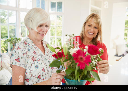 Senior donna e figlia adulta disponendo dei fiori a casa Foto Stock