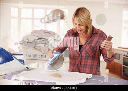 Distratti donna di mezza età ustioni t shirt durante la stiratura Foto Stock