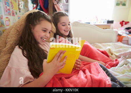 Due sorelle lettura libro seduti sul letto insieme Foto Stock