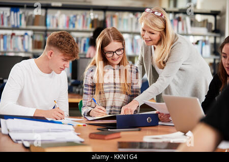 Insegnante femminile lavora con studenti di college in libreria Foto Stock