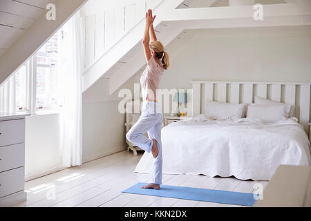 La donna a casa la mattina partenza con esercizi di yoga in camera da letto Foto Stock