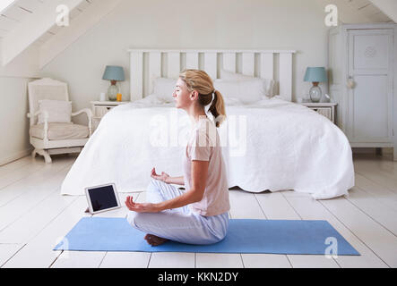 Donna con tavoletta digitale utilizzando la meditazione di app in camera da letto Foto Stock