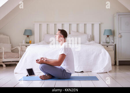 Uomo maturo con tavoletta digitale utilizzando la meditazione di app in camera da letto Foto Stock