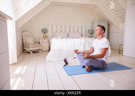 Uomo maturo con tavoletta digitale utilizzando la meditazione di app in camera da letto Foto Stock
