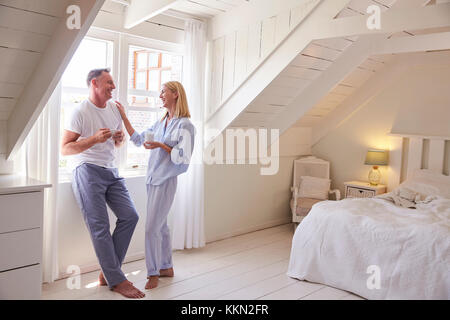 Coppia Matura in piedi dalla finestra della camera con bevanda calda Foto Stock