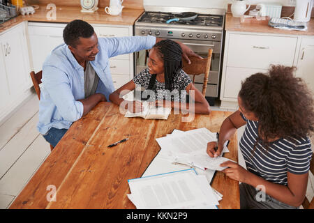 Aiutando il padre di due figlie seduta a tavola facendo i compiti di scuola Foto Stock