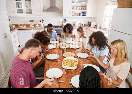 Due famiglie dicendo grazia prima di mangiare mangiare insieme Foto Stock