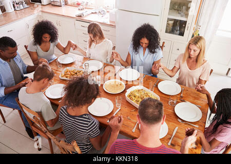 Due famiglie dicendo grazia prima di mangiare mangiare insieme Foto Stock