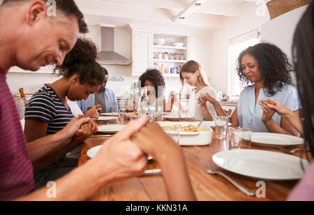 Due famiglie dicendo grazia prima di mangiare mangiare insieme Foto Stock