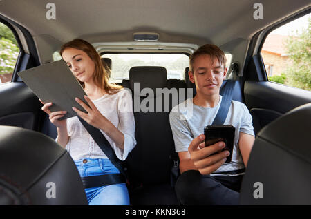 Figli adolescenti utilizzando dispositivi digitali su Famiglia Viaggio su strada Foto Stock