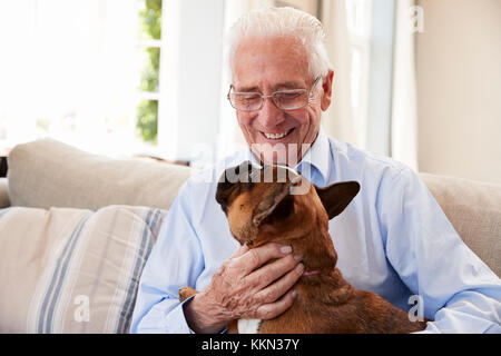 Senior uomo seduto sul divano di casa con Pet bulldog francese Foto Stock