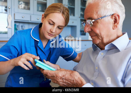 Infermiere Senior aiuta l uomo a organizzare i medicamenti sulla Home Visita Foto Stock