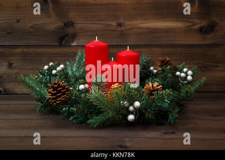 Decorate corona di Avvento con tre candele rosse su uno sfondo di legno. Foto Stock