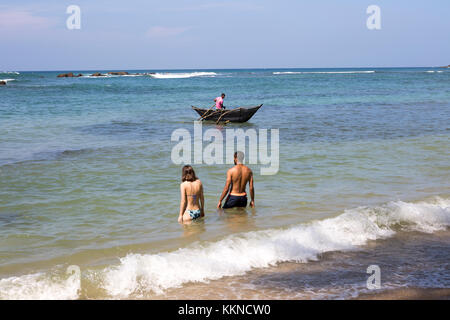 I turisti di balneazione in mare Pesca uomo utilizzando tradizionali canoe outrigger, Mirissa, Sri Lanka, Asia Foto Stock