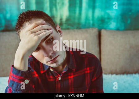 Profilo laterale ha sottolineato triste pianto giovane uomo seduto fuori tenendo la testa con le mani guardando giù. emozione umana sentimenti. in un cattivo umore. cefalea, testa Foto Stock