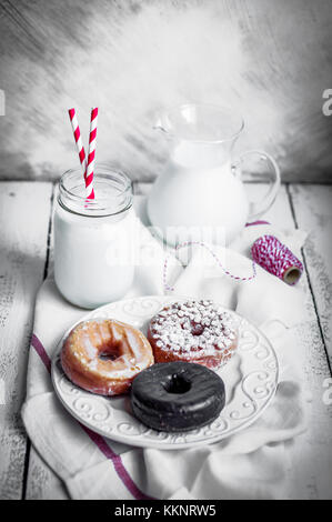 Latte e ciambelle assortite sul rustico sfondo di legno Foto Stock