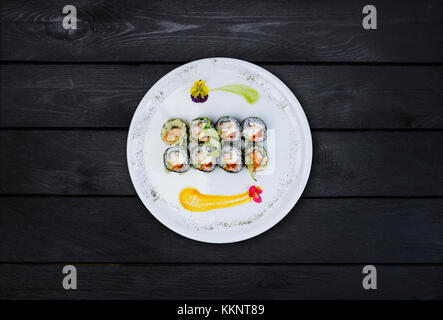 Sushi fritto con un cetriolo, alcuni di crema di formaggio, tobiko caviar e gamberetti. vista dall'alto. nero lo sfondo di legno Foto Stock