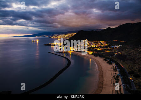 Vista del tramonto di splendidamente illuminate San Andres cittadina con la città capitale Santa Cruz de Tenerife in background, spiaggia di Las Teresitas in primo piano e Foto Stock