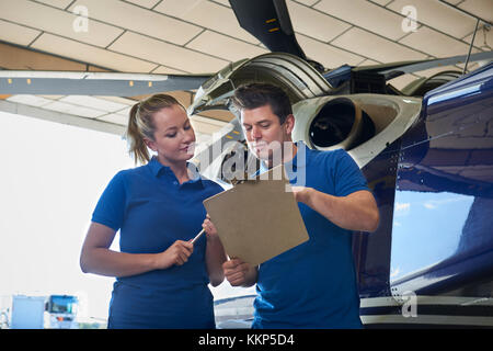 Aero ingegnere e apprendista Lavorare in elicottero in hangar guardando negli appunti Foto Stock