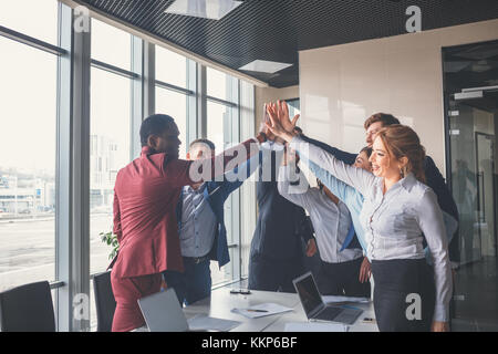 Team aziende fornendo un alto cinque gesto come ridono e allietare il loro successo Foto Stock