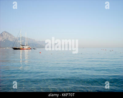 Kemer Antalia bella vista sul mare. Spiaggia Kemer Antalia con sabbia e montagne, il mare con la nave. Bellissimo porto vicino alla spiaggia di sabbia. Foto Stock