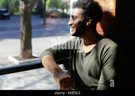L'uomo spagnolo seduto al bar e ridendo al rallentatore, mette la tazza sul tavolo. Il ragazzo ha i capelli neri, la barba e le fossette sulle guance. Concetto di caffè gustoso Go Foto Stock