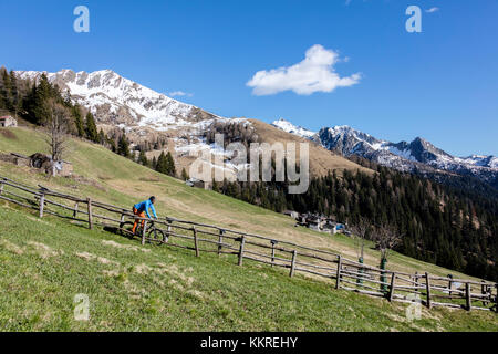 In mountain bike sui prati verdi incorniciato da vette innevate in primavera albaredo valle alpi Orobie valtellina lombardia italia Europa Foto Stock