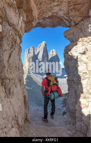 Escursionista cercando le tre cime di lavaredo / Drei Zinnen attraverso una finestra nella roccia ai piedi del monte paterno / paternkofel, sesto dolomiti alto adige, bolzano, Italia Foto Stock