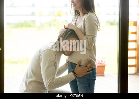 Uomo felice mettendo orecchio alla moglie incinta ventre a casa Foto Stock