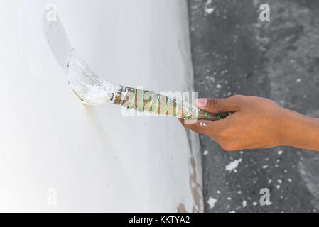 Pittura pareti.Pittore dipinge utilizzando una spazzola,mano lavoratore azienda verniciatura a pennello bianco su parete in cemento, e soft-focus sullo sfondo (selezionare focus tenere in mano Foto Stock