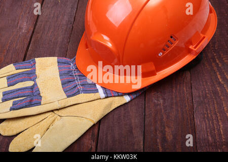 Orange elmetto, occhiali di sicurezza e guanti protettivi e nastro di misurazione su sfondo di legno. Foto Stock