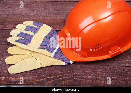 Orange elmetto, occhiali di sicurezza e guanti protettivi e nastro di misurazione su sfondo di legno. Foto Stock