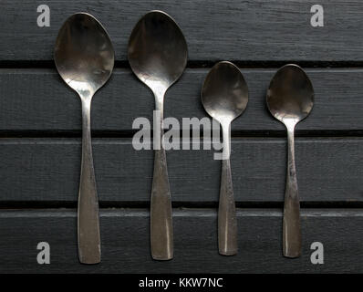 Set di quattro cucchiai di argento sulla parte superiore di un legno nero lo sfondo della superficie del piano portapaziente, allineati e organizzato Foto Stock