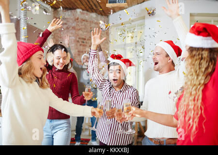 Entusiasta di ragazzi e ragazze la tostatura con flauti di champagne mentre festeggia il Natale a casa Foto Stock