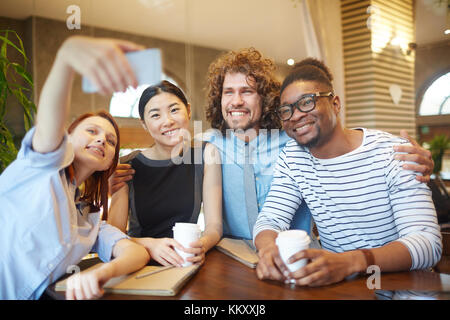 Giovani studenti interculturale o direttori che fanno selfie in cafe mentre seduta al tavolo a coffee-break Foto Stock