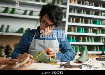 Professional cobbler prendendo misure dal boot incompiuta dal suo luogo di lavoro Foto Stock