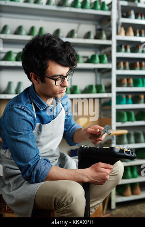 Il comando cobbler con utensili tenendo i chiodi da suola per calzatura durante la riparazione di esso Foto Stock