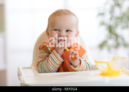 Happy baby boy in attesa di cibo con cucchiaio a tavola Foto Stock