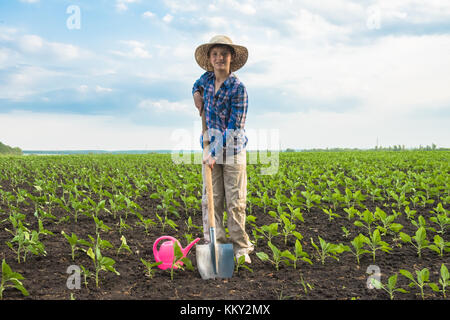 Felice piccolo agricoltore con spade e annaffiatoio in campo primaverile del giardinaggio Foto Stock