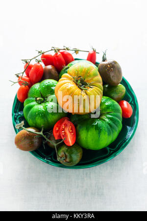 Tipi diversi tipi e colori di pomodori in un bianco tavolo di pietra. ingredienti per il mangiare sano: ciliegia, nero krim, kumato, big rainbow , verde Foto Stock