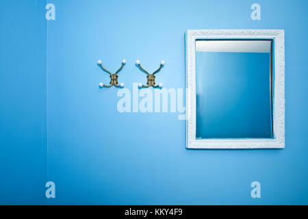 Due appendiabiti e uno specchio su una parete blu Foto Stock