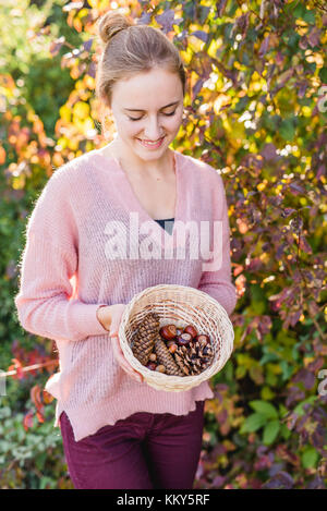 Giardino, giovane donna con cesto di raccolta di materiali naturali, Foto Stock