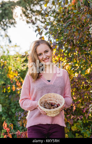 Giardino, giovane donna con cesto di raccolta di materiali naturali, Foto Stock