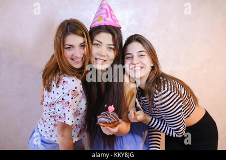 Allegro e bellissima femmina amici ridere e sorridere, due ragazze mi congratulo con brunette sul compleanno di festa con il cappuccio sulla testa che detiene ciambella al cioccolato Foto Stock