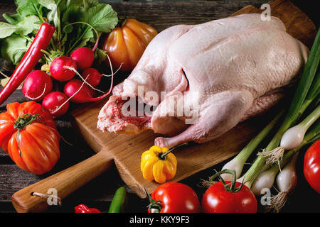 Materie giovane anatra sul tagliere di legno con fresche e mature le verdure sopra un tavolo di legno. oscura atmosfera rustica. Foto Stock