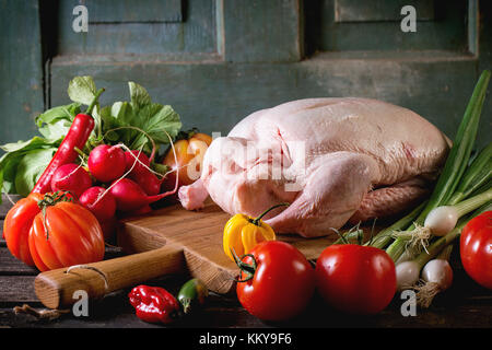 Materie giovane anatra sul tagliere di legno con fresche e mature le verdure sopra un tavolo di legno. oscura atmosfera rustica. Foto Stock